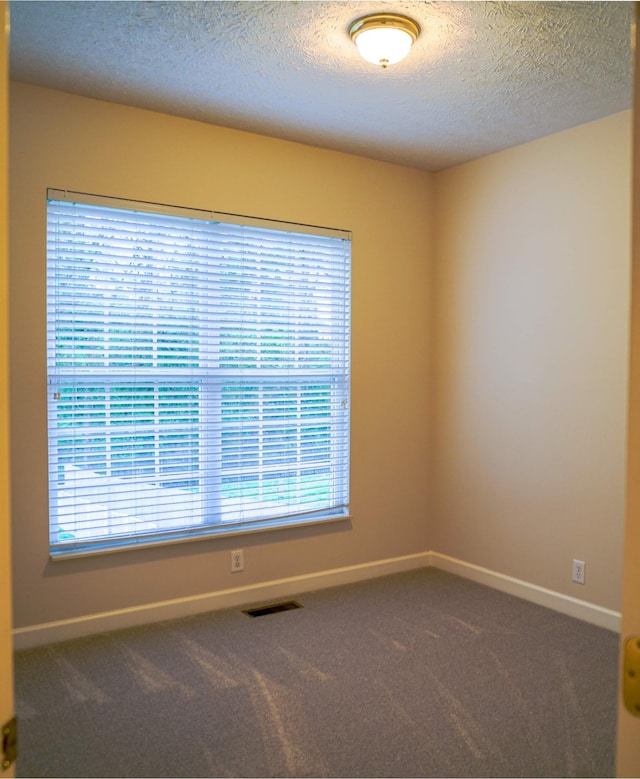 empty room featuring carpet flooring, visible vents, a textured ceiling, and baseboards