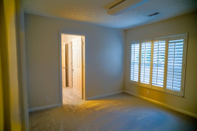 carpeted empty room featuring a textured ceiling, baseboards, and visible vents