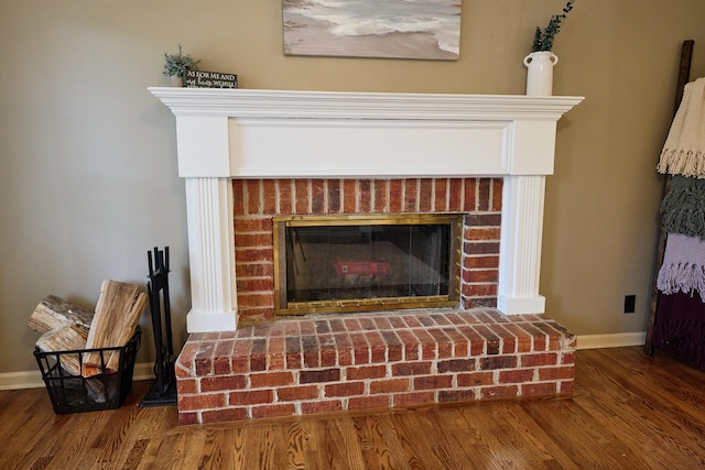 room details featuring a brick fireplace, baseboards, and wood finished floors