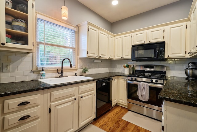kitchen featuring a sink, black appliances, dark stone counters, and light wood-style floors