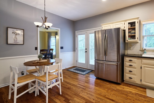 interior space with plenty of natural light, an inviting chandelier, freestanding refrigerator, wainscoting, and wood finished floors