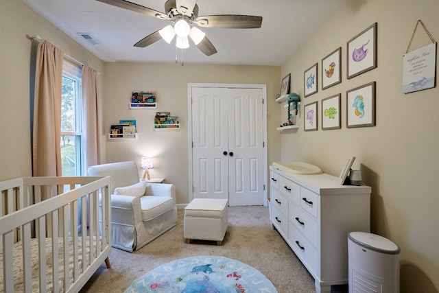 bedroom with a closet, a crib, light carpet, a ceiling fan, and visible vents