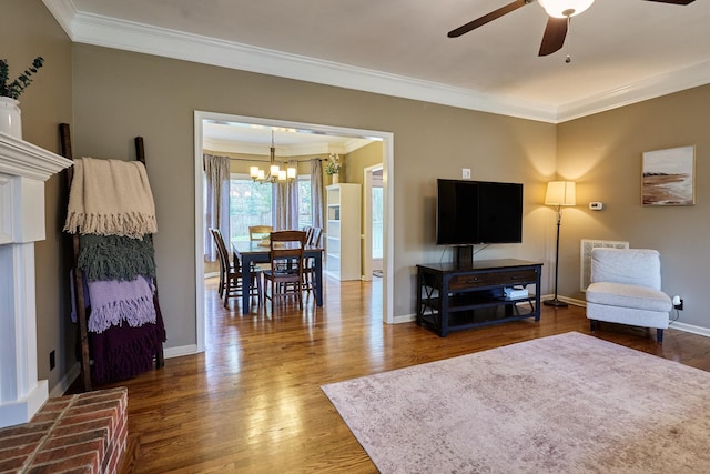 living area featuring baseboards, ceiling fan with notable chandelier, crown molding, and wood finished floors