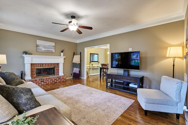 living room featuring baseboards, a brick fireplace, ornamental molding, ceiling fan, and wood finished floors