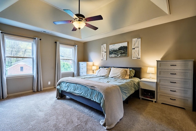 carpeted bedroom with visible vents, a tray ceiling, baseboards, and ceiling fan