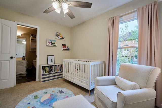 carpeted bedroom featuring ceiling fan and a crib