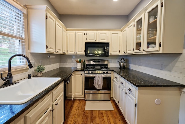 kitchen with glass insert cabinets, black appliances, wood finished floors, a sink, and backsplash