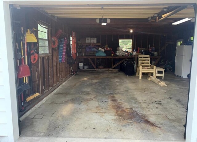 garage with a garage door opener, freestanding refrigerator, and a workshop area