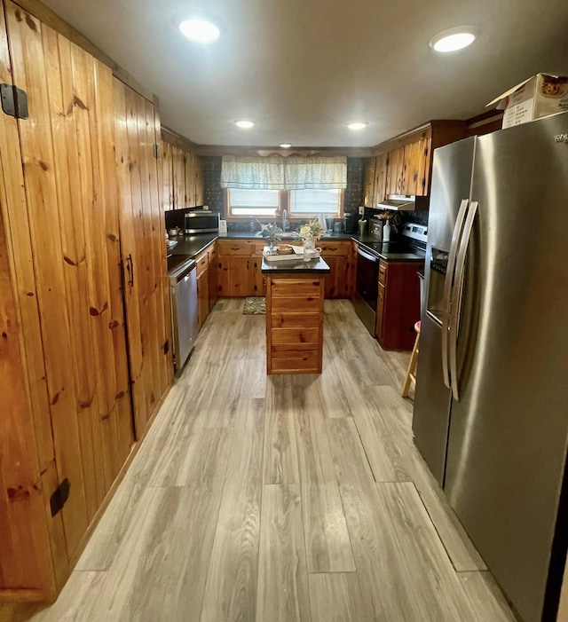 kitchen featuring dark countertops, light wood-style floors, under cabinet range hood, brown cabinets, and stainless steel appliances
