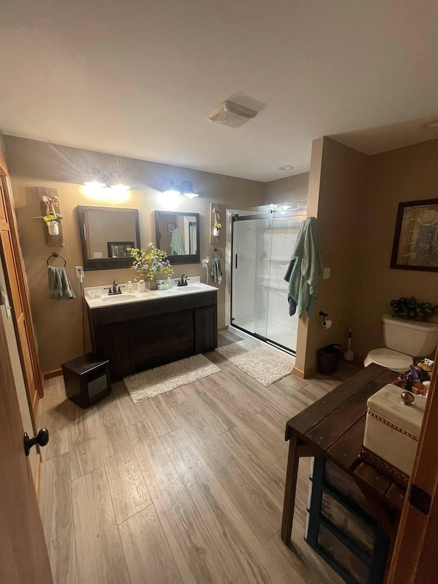 bathroom featuring a sink, a shower stall, double vanity, and wood finished floors