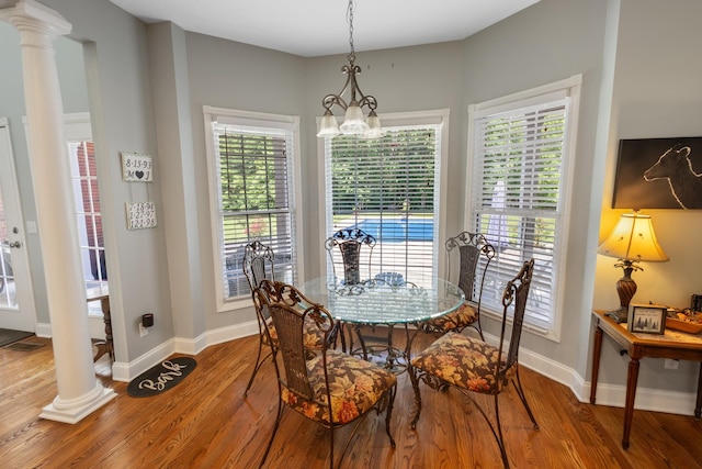 dining space with ornate columns, wood finished floors, a notable chandelier, and a wealth of natural light
