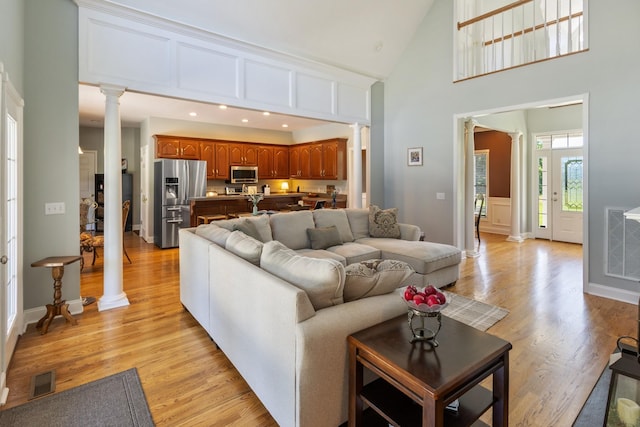 living room with light wood-style flooring, decorative columns, and high vaulted ceiling