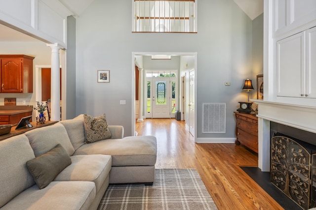 living room with high vaulted ceiling, light wood-style flooring, ornate columns, visible vents, and baseboards