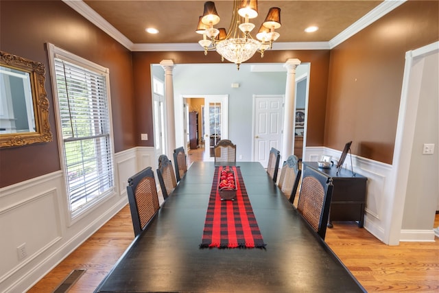 dining area with light wood-style floors, an inviting chandelier, ornate columns, ornamental molding, and a wainscoted wall