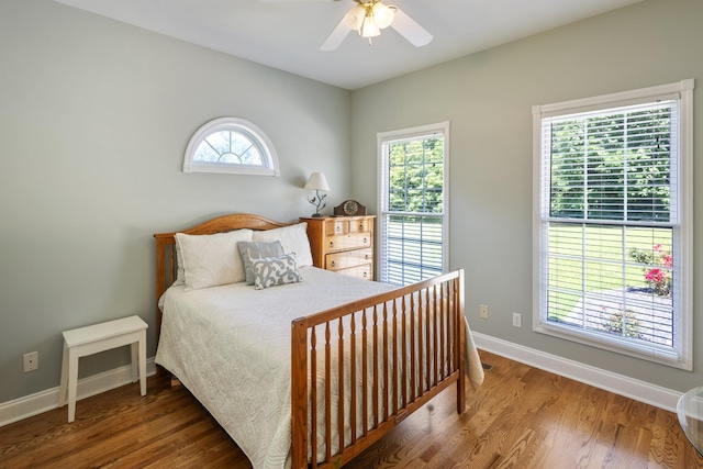 bedroom featuring a ceiling fan, wood finished floors, baseboards, and multiple windows