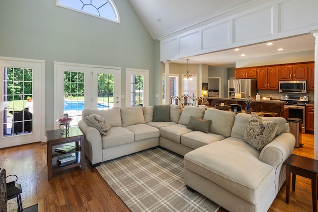 living room featuring a notable chandelier, dark wood-style floors, ornate columns, recessed lighting, and high vaulted ceiling