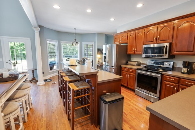 kitchen with light wood finished floors, appliances with stainless steel finishes, decorative columns, and a breakfast bar