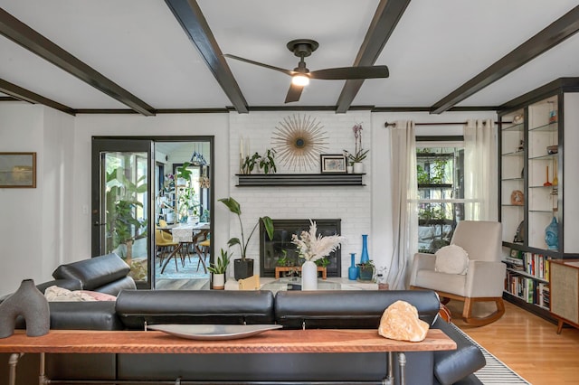 living area with beamed ceiling, a brick fireplace, wood finished floors, and ceiling fan
