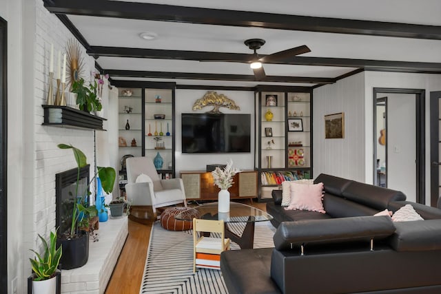 living area featuring wood finished floors, a fireplace, beamed ceiling, and ceiling fan