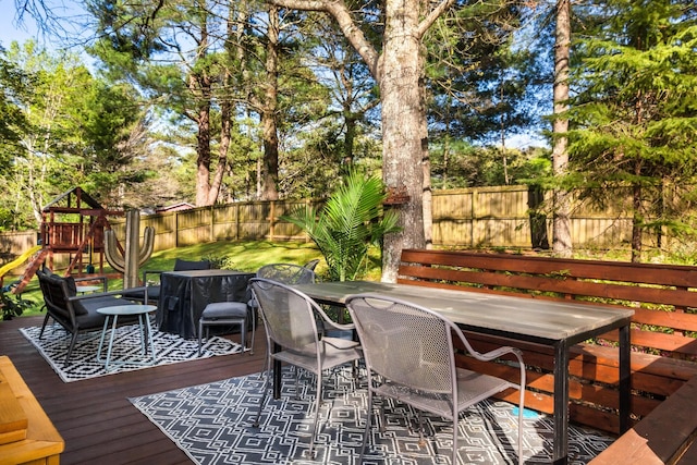 deck with a fenced backyard, outdoor dining space, and a playground