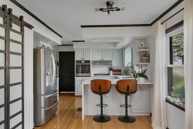 kitchen with a peninsula, appliances with stainless steel finishes, under cabinet range hood, light countertops, and a sink