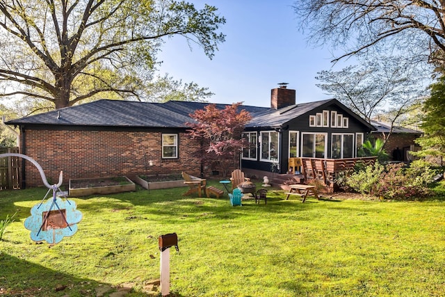 rear view of house featuring a sunroom, a chimney, a shingled roof, and a lawn