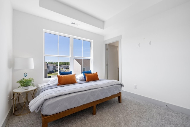 bedroom with a tray ceiling, carpet flooring, baseboards, and visible vents
