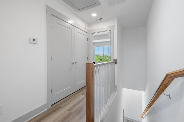 hall with visible vents, an upstairs landing, attic access, and light wood finished floors