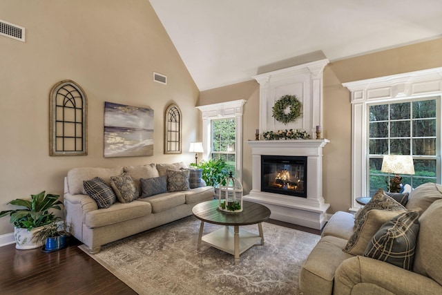 living area with a large fireplace, visible vents, high vaulted ceiling, and wood finished floors