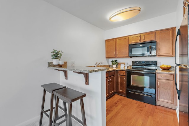 801 Inverness Ave Unit B1, Nashville, TN 37204 - kitchen featuring black appliances, a breakfast bar, a peninsula, light wood finished floors, and light stone countertops
