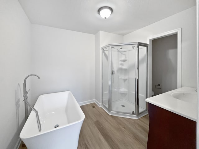 bathroom featuring vanity, wood finished floors, a freestanding bath, a stall shower, and baseboards