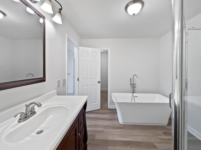full bathroom with vanity, a soaking tub, and wood finished floors