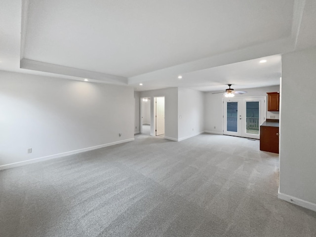 unfurnished living room with a raised ceiling, recessed lighting, baseboards, and ceiling fan
