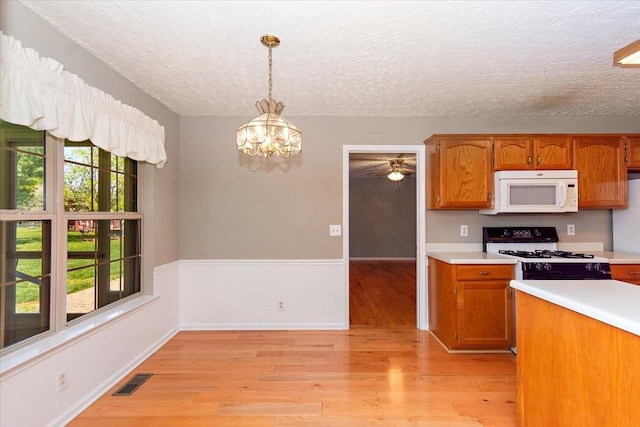 kitchen with a textured ceiling, white appliances, light wood-type flooring, light countertops, and visible vents