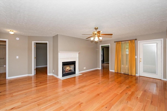 unfurnished living room with light wood-type flooring, a textured ceiling, a ceiling fan, and baseboards