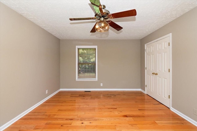 empty room featuring light wood-style flooring, baseboards, and a textured ceiling