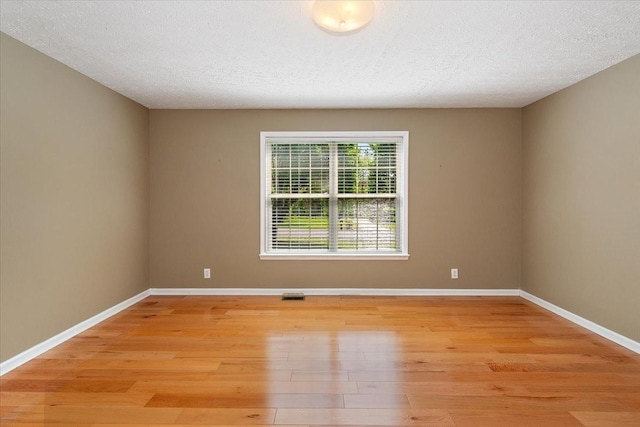 spare room with baseboards, light wood-style floors, visible vents, and a textured ceiling