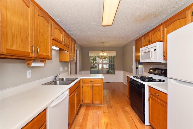 kitchen featuring light countertops, a sink, white appliances, a peninsula, and light wood-style flooring
