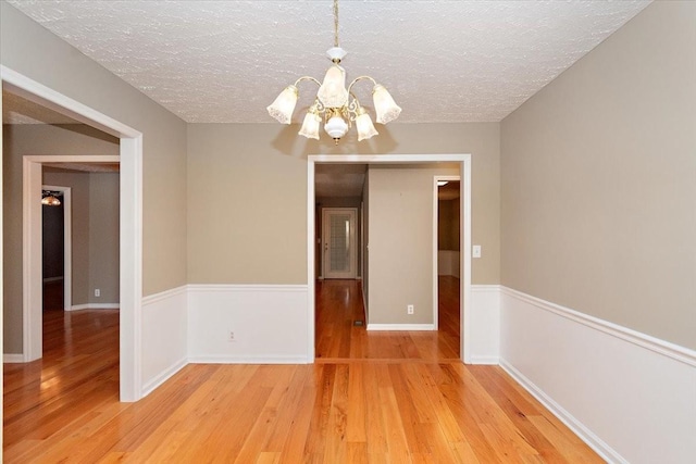 empty room featuring light wood-style floors, a textured ceiling, baseboards, and a notable chandelier