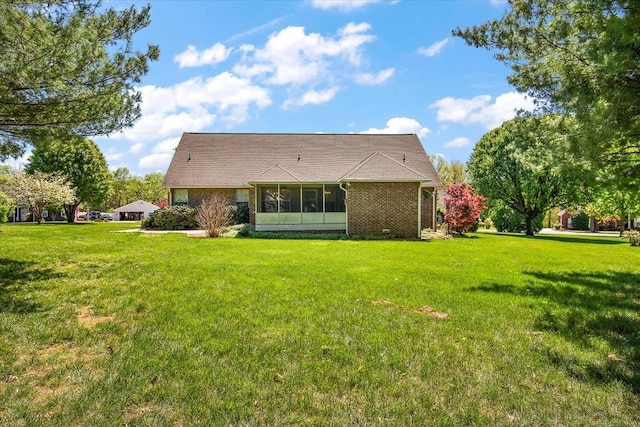 back of property with a sunroom, a yard, and brick siding