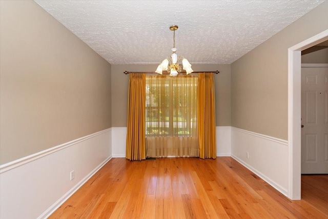 empty room with baseboards, a chandelier, a textured ceiling, and light wood-style flooring