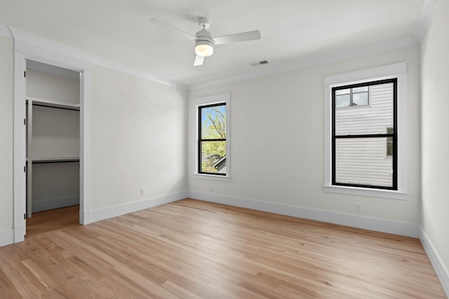 unfurnished bedroom featuring baseboards, a spacious closet, crown molding, ceiling fan, and light wood finished floors