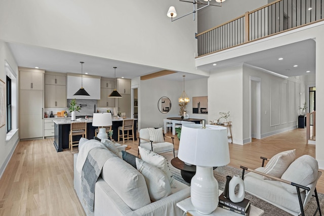 living room featuring a chandelier, light wood-type flooring, a towering ceiling, and recessed lighting