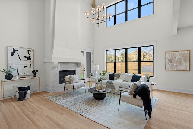 living area with baseboards, a notable chandelier, wood finished floors, and a high end fireplace