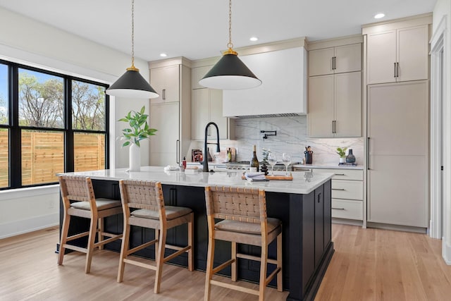 kitchen with tasteful backsplash, an island with sink, light wood-style flooring, a breakfast bar area, and hanging light fixtures