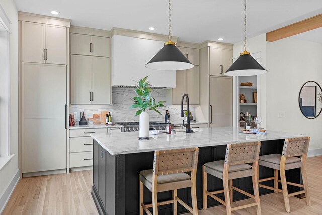 kitchen with tasteful backsplash, light wood-type flooring, a breakfast bar, a center island with sink, and light stone countertops
