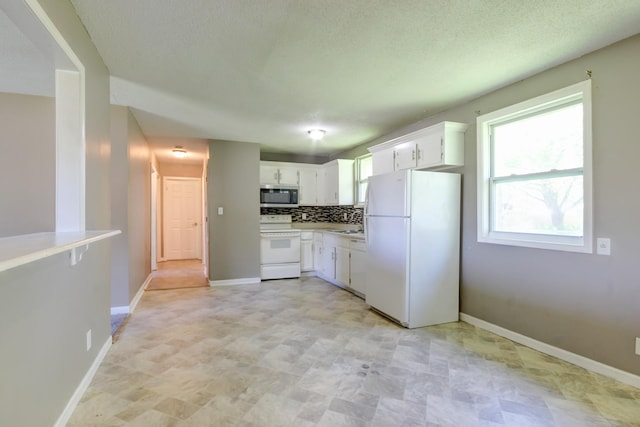 kitchen with baseboards, light countertops, white appliances, and white cabinetry
