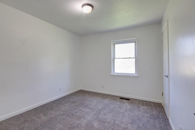 carpeted empty room featuring a textured ceiling, visible vents, and baseboards