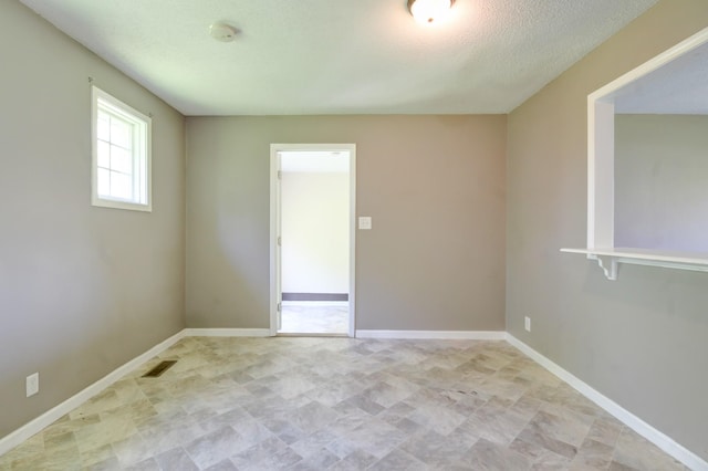 spare room with baseboards, a textured ceiling, and visible vents