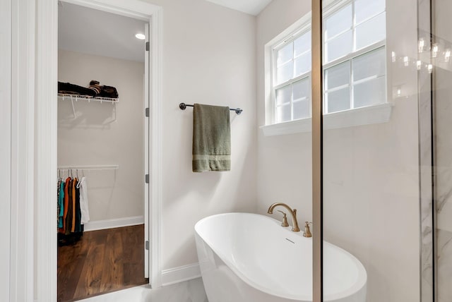 full bath featuring baseboards, a soaking tub, a walk in closet, a shower, and wood finished floors